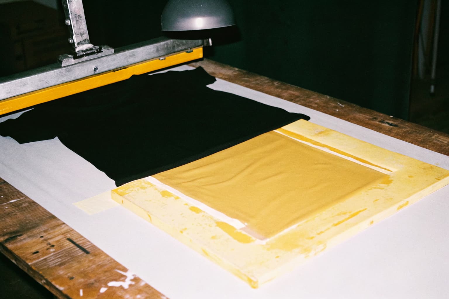 A single black t-shirt mid-print on an in-house screen press, no minimum order