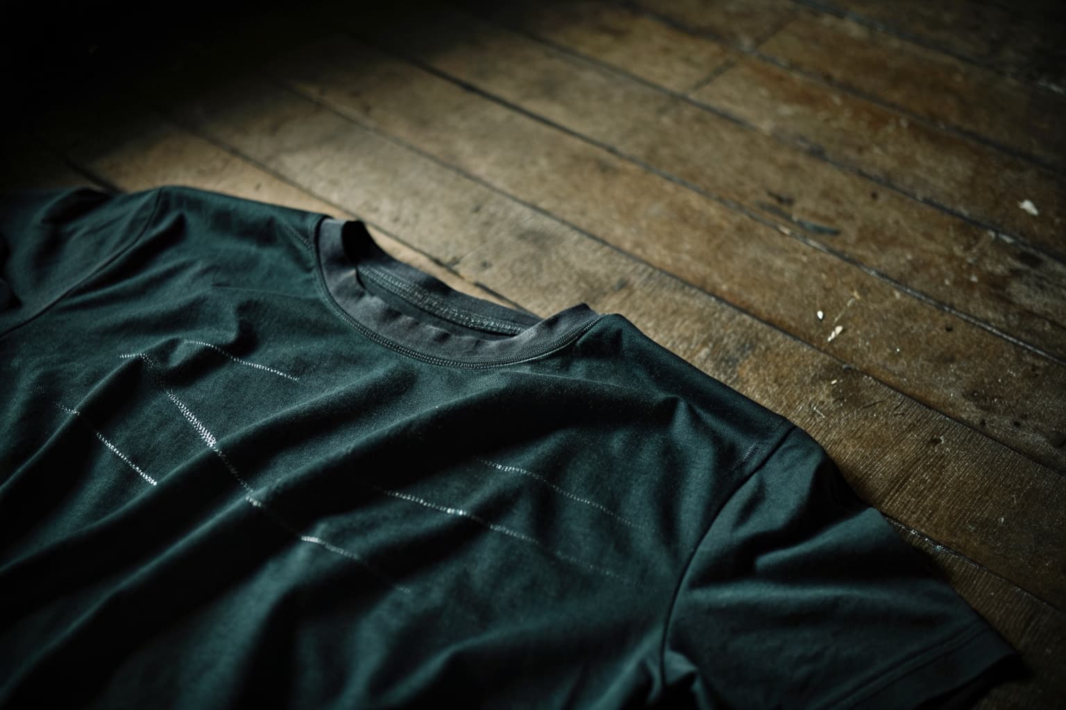 Close-up of a black screen printed shirt laid on a dark wood plank, showing crisp unbroken ink after a full season of wear